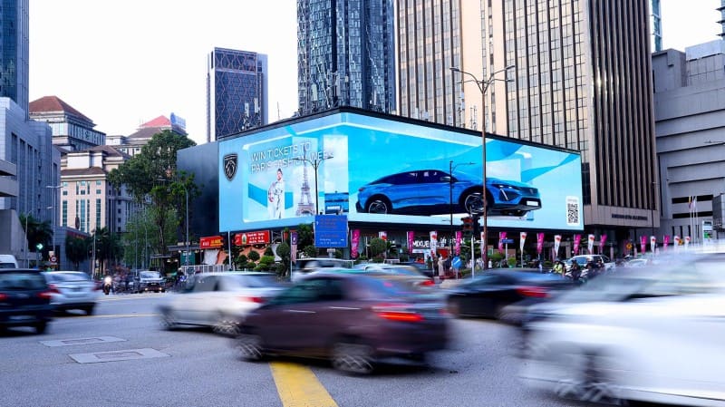 A large digital billboard showing a car ad above traffic at a junction in Kuala Lumpur
